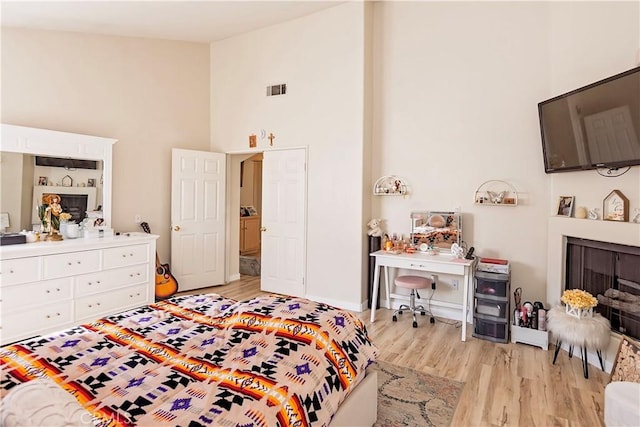 bedroom featuring high vaulted ceiling, light wood-style flooring, a fireplace, and visible vents