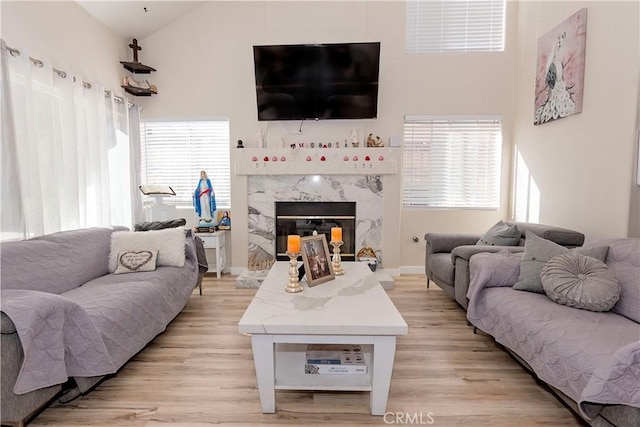 living room featuring light wood-style floors, a premium fireplace, and high vaulted ceiling