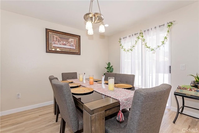 dining area with light wood-type flooring, a notable chandelier, and baseboards