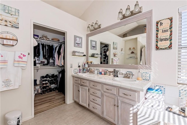 bathroom with double vanity, lofted ceiling, wood finished floors, a spacious closet, and a sink