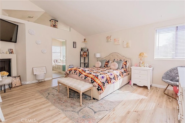 bedroom with a fireplace, vaulted ceiling, ensuite bath, wood finished floors, and baseboards