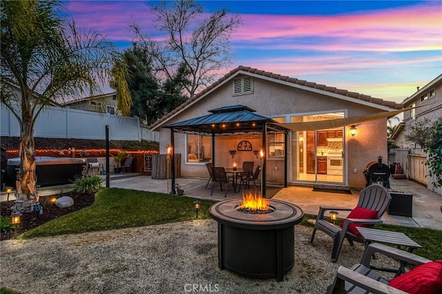 back of property featuring an outdoor fire pit, a patio, a fenced backyard, a gazebo, and stucco siding