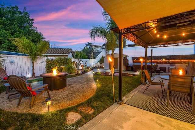 patio terrace at dusk with a fire pit, a gazebo, and a fenced backyard