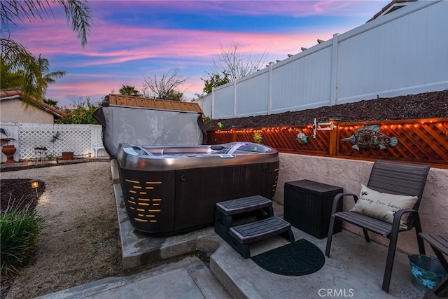 patio terrace at dusk featuring a fenced backyard and a hot tub