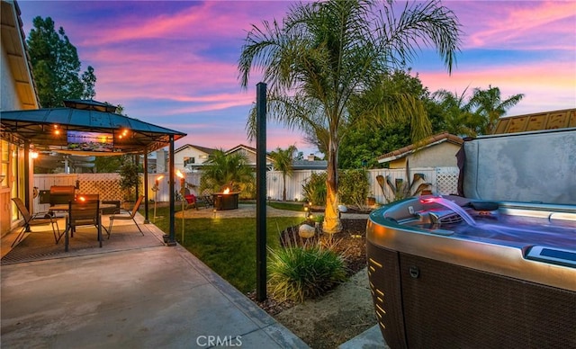 patio terrace at dusk featuring outdoor dining space, a fenced backyard, a lawn, and a gazebo