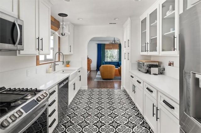 kitchen featuring arched walkways, stainless steel appliances, a sink, white cabinets, and glass insert cabinets