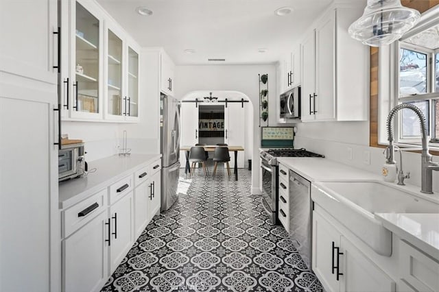 kitchen with appliances with stainless steel finishes, a barn door, a sink, and white cabinetry