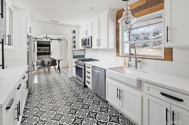 kitchen with arched walkways, stainless steel appliances, light countertops, white cabinetry, and a sink