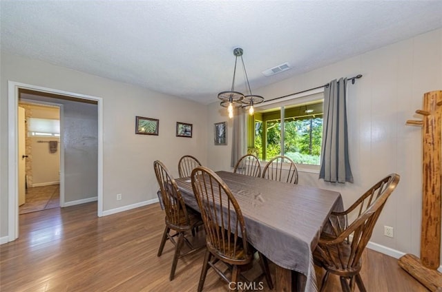 dining room with visible vents, a textured ceiling, wood finished floors, an inviting chandelier, and baseboards