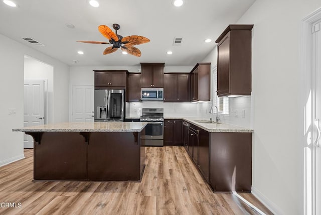 kitchen featuring a breakfast bar area, stainless steel appliances, a sink, visible vents, and dark brown cabinets