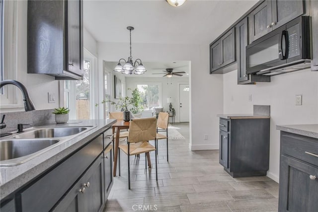 kitchen featuring black microwave, light wood-style flooring, a sink, baseboards, and decorative light fixtures