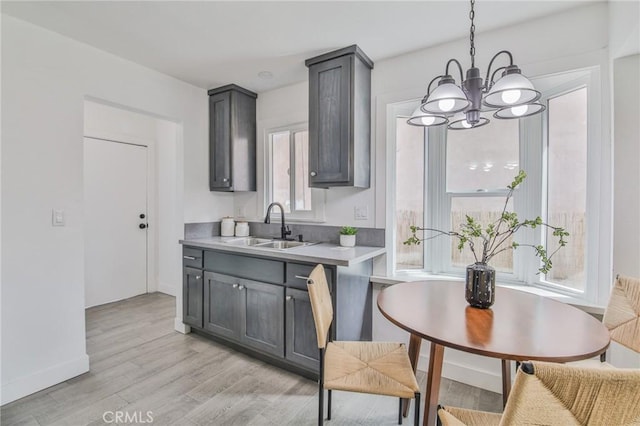 kitchen with baseboards, hanging light fixtures, light countertops, light wood-style floors, and a sink