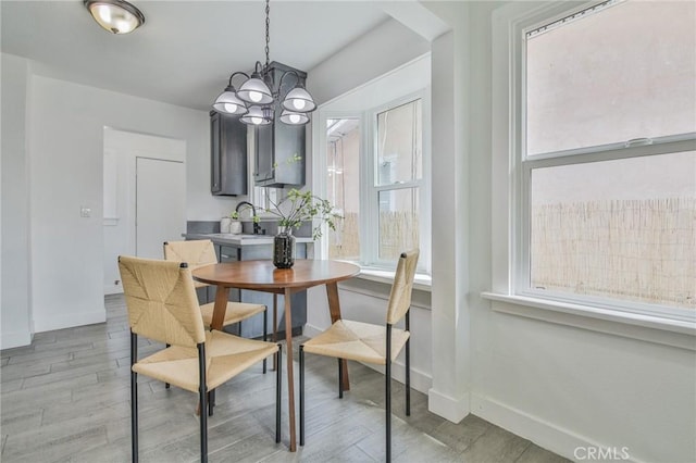 dining area with baseboards, light wood-type flooring, plenty of natural light, and a notable chandelier