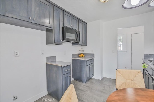 kitchen with black microwave, light countertops, light wood-style flooring, and baseboards