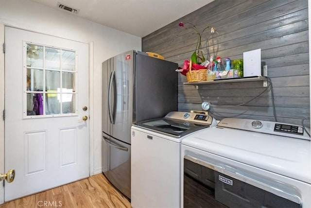 washroom with washing machine and dryer, light wood-style flooring, wooden walls, laundry area, and visible vents