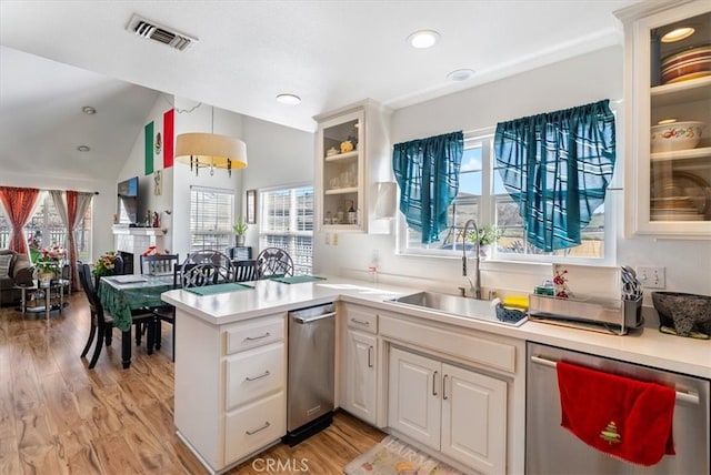 kitchen with light countertops, visible vents, glass insert cabinets, a sink, and dishwasher