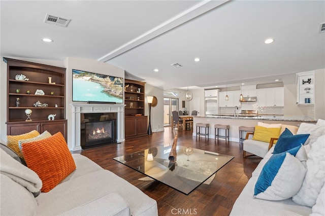 living area with visible vents, dark wood-type flooring, and a glass covered fireplace