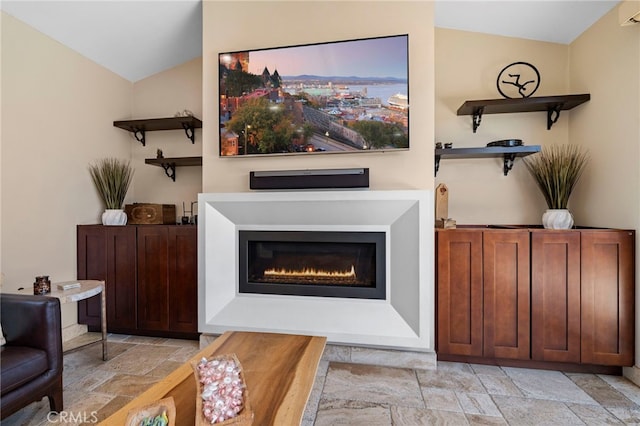 interior space with vaulted ceiling, a glass covered fireplace, and stone tile flooring