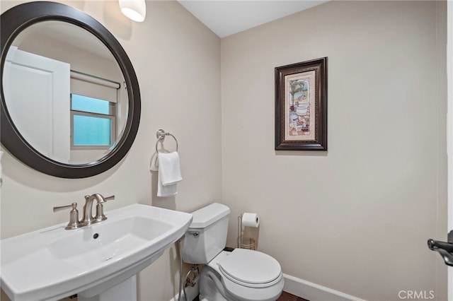 half bathroom featuring toilet, baseboards, and a sink