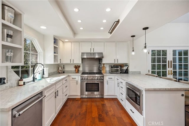 kitchen with open shelves, stainless steel appliances, a raised ceiling, a peninsula, and under cabinet range hood