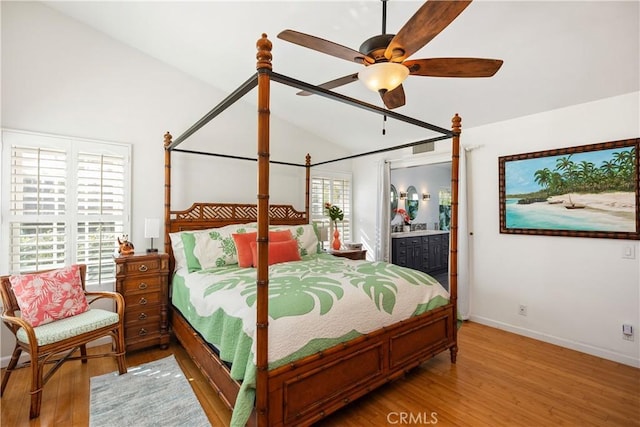 bedroom featuring baseboards, vaulted ceiling, wood finished floors, and ensuite bathroom