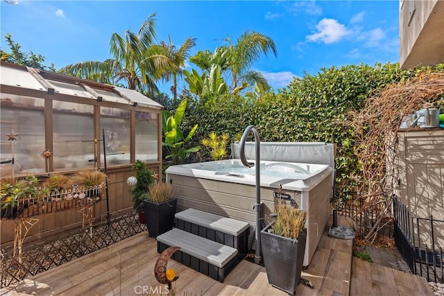 wooden deck with a greenhouse, a hot tub, and an outbuilding