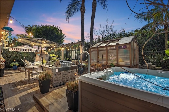 patio terrace at dusk featuring an outbuilding, an exterior structure, and a hot tub