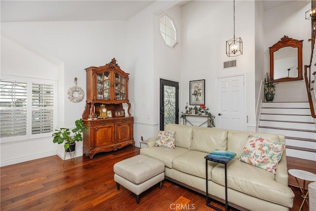 living area with visible vents, stairs, a wealth of natural light, dark wood-style floors, and an inviting chandelier