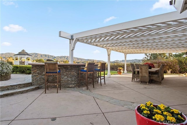 view of patio featuring outdoor dry bar, outdoor dining space, a mountain view, and a pergola