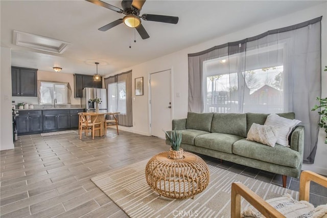 living area with baseboards, light wood-style flooring, attic access, and a ceiling fan