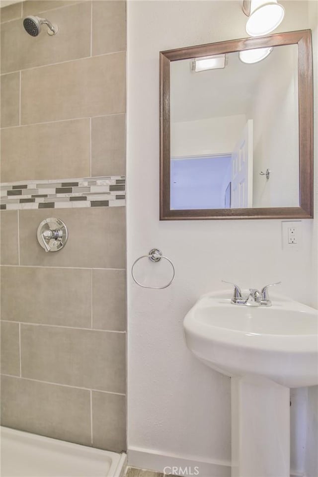 full bathroom featuring a tile shower and a sink