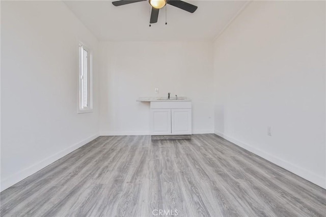 spare room featuring light wood finished floors, a sink, a ceiling fan, and baseboards