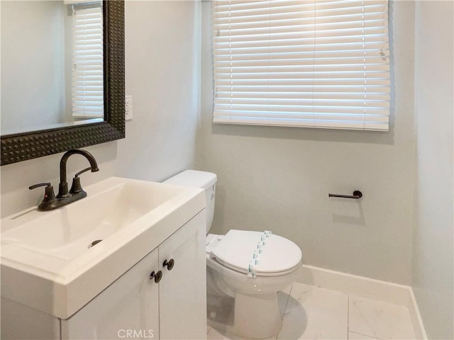 half bath with baseboards, vanity, and toilet