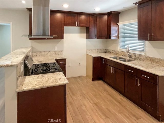 kitchen featuring island range hood, a sink, light stone countertops, light wood finished floors, and gas stove