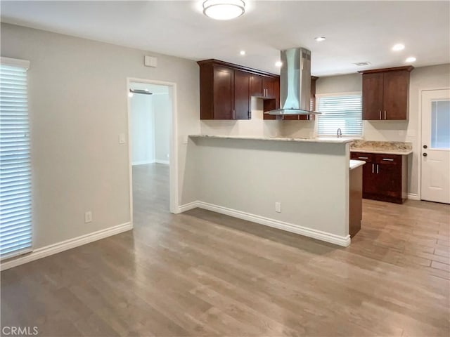 kitchen with light countertops, dark brown cabinetry, island range hood, light wood-type flooring, and baseboards