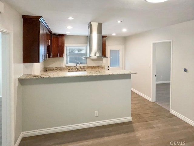 kitchen featuring a sink, wall chimney range hood, dark brown cabinets, wood finished floors, and baseboards