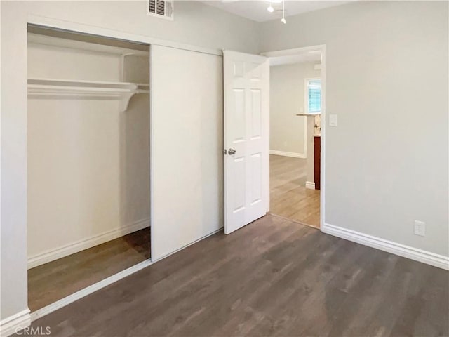 unfurnished bedroom with baseboards, visible vents, dark wood finished floors, and a closet