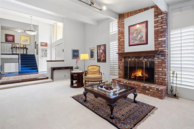 carpeted living area with stairway, a brick fireplace, and beam ceiling