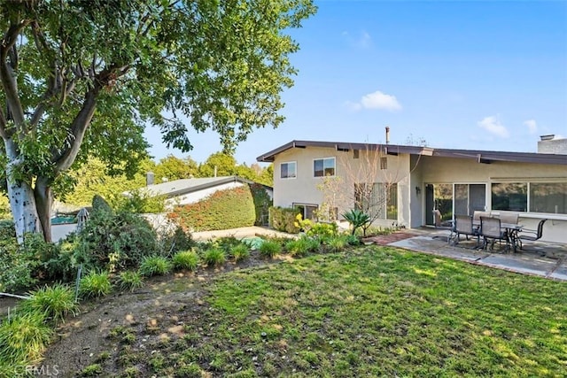 rear view of house featuring stucco siding, a lawn, and a patio