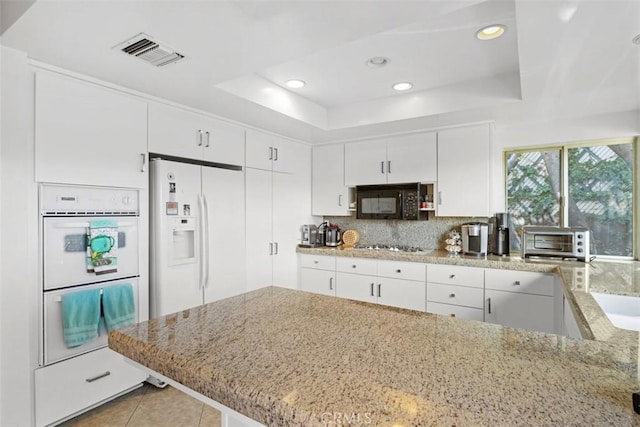 kitchen featuring a tray ceiling, a toaster, visible vents, light stone countertops, and white appliances