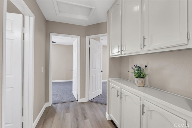 hallway featuring baseboards, attic access, and light wood-style floors