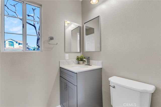 half bath featuring toilet, a textured wall, and vanity