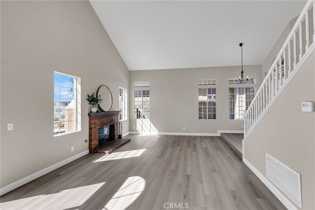 unfurnished living room featuring a chandelier, high vaulted ceiling, a fireplace, visible vents, and light wood-style floors