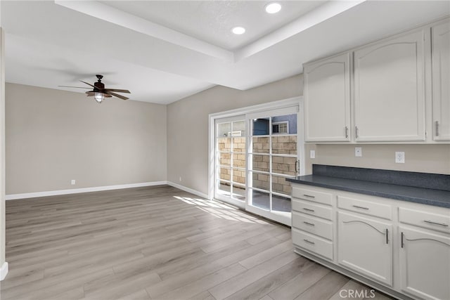 kitchen with baseboards, white cabinets, dark countertops, a tray ceiling, and light wood-style floors