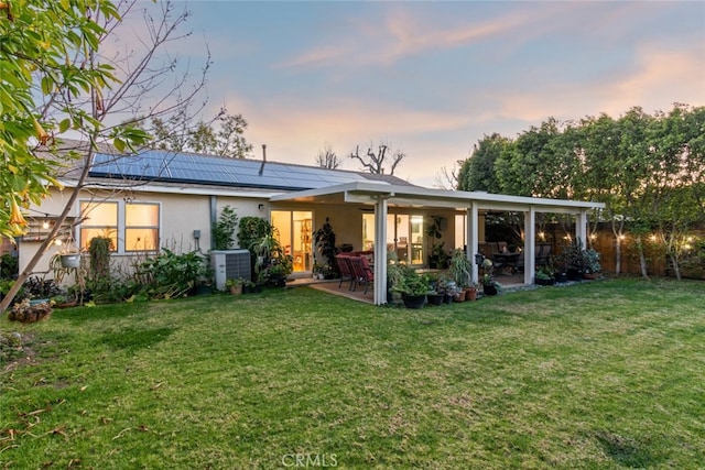 back of property featuring stucco siding, roof mounted solar panels, central AC, a yard, and a patio area