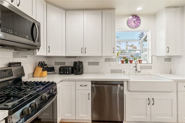 kitchen with a sink, backsplash, white cabinetry, appliances with stainless steel finishes, and light stone countertops