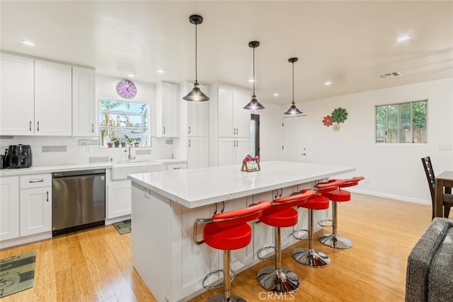 kitchen with light wood finished floors, visible vents, stainless steel dishwasher, white cabinets, and a sink