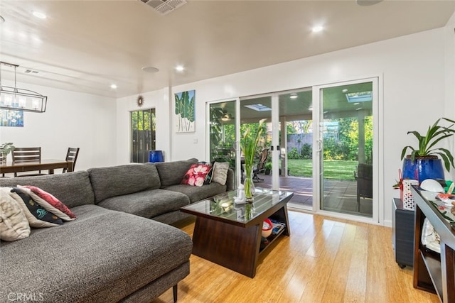 living area with visible vents, plenty of natural light, an inviting chandelier, and light wood-style flooring