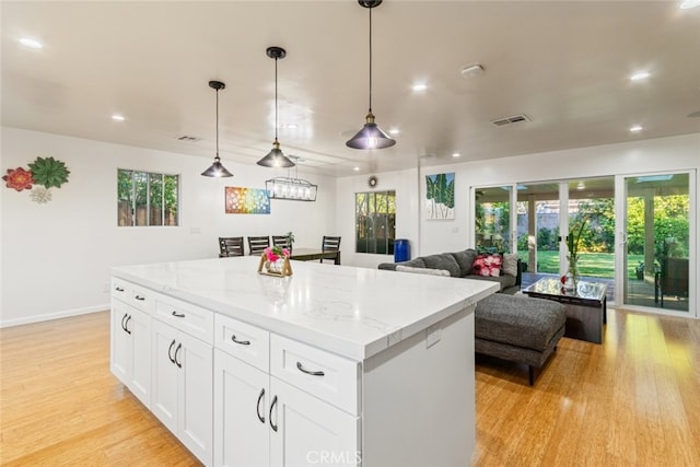 kitchen with light stone countertops, visible vents, a kitchen island, white cabinets, and light wood-type flooring