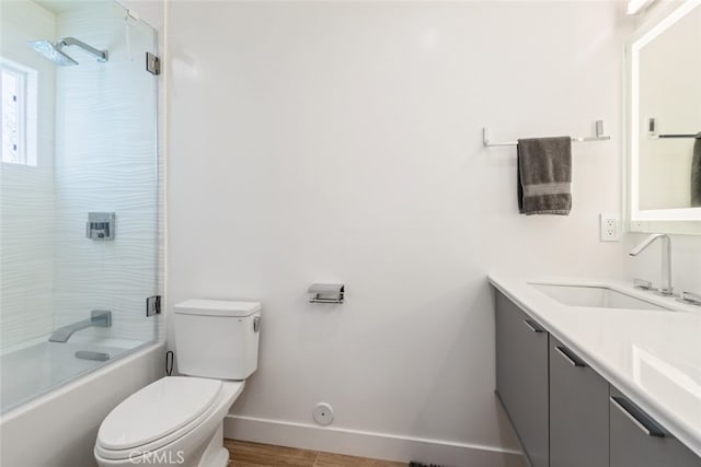 full bath featuring vanity, wood finished floors, baseboards, bath / shower combo with glass door, and toilet